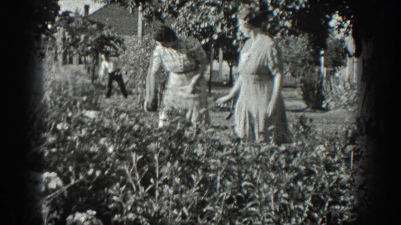 1936 California 8mm frame showing two older women in a garden, with a man working farther back near trees and low buildings.