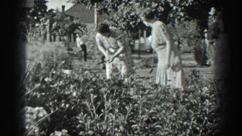 1936 California home-movie frame showing two older women tending a lush garden, with a man farther back in the yard.