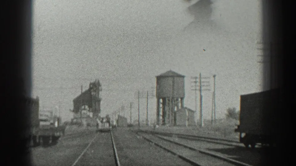 1936 California rail yard view with tracks, a wooden water tower, freight cars, utility poles, and small distant figures.