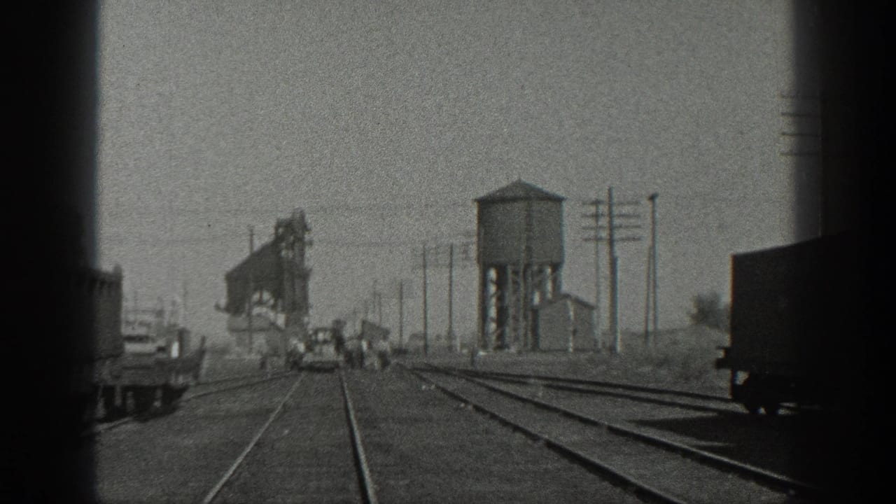 1936 California rail-yard view with converging tracks, distant people near a small rail car, utility poles, and a water tower-like structure.
