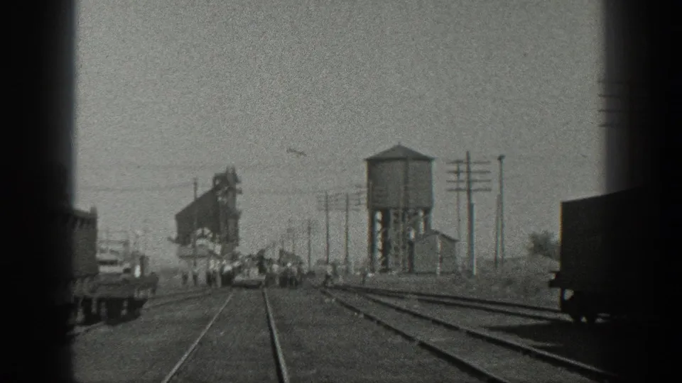 1936 California rail-yard view with several distant people around a small rail car, multiple tracks, utility poles, and industrial structures.