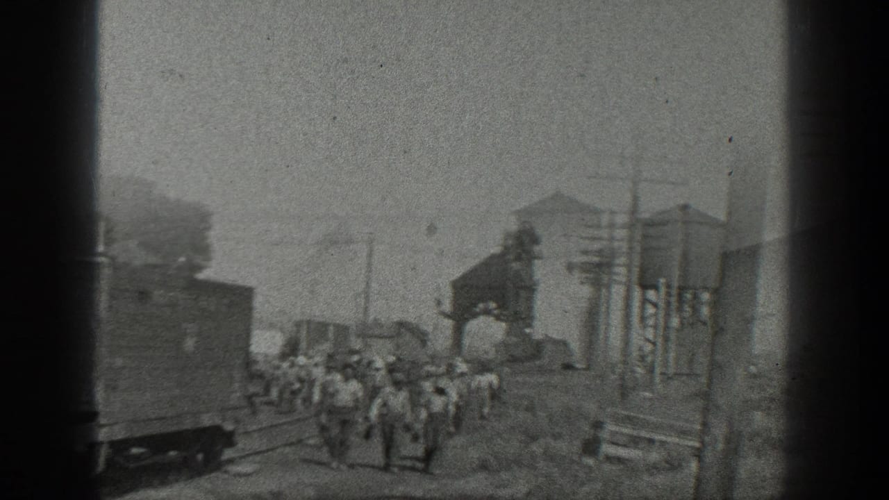1936 California home-movie frame showing workers walking through a rail yard with freight cars, tracks, utility poles, and industrial structures.