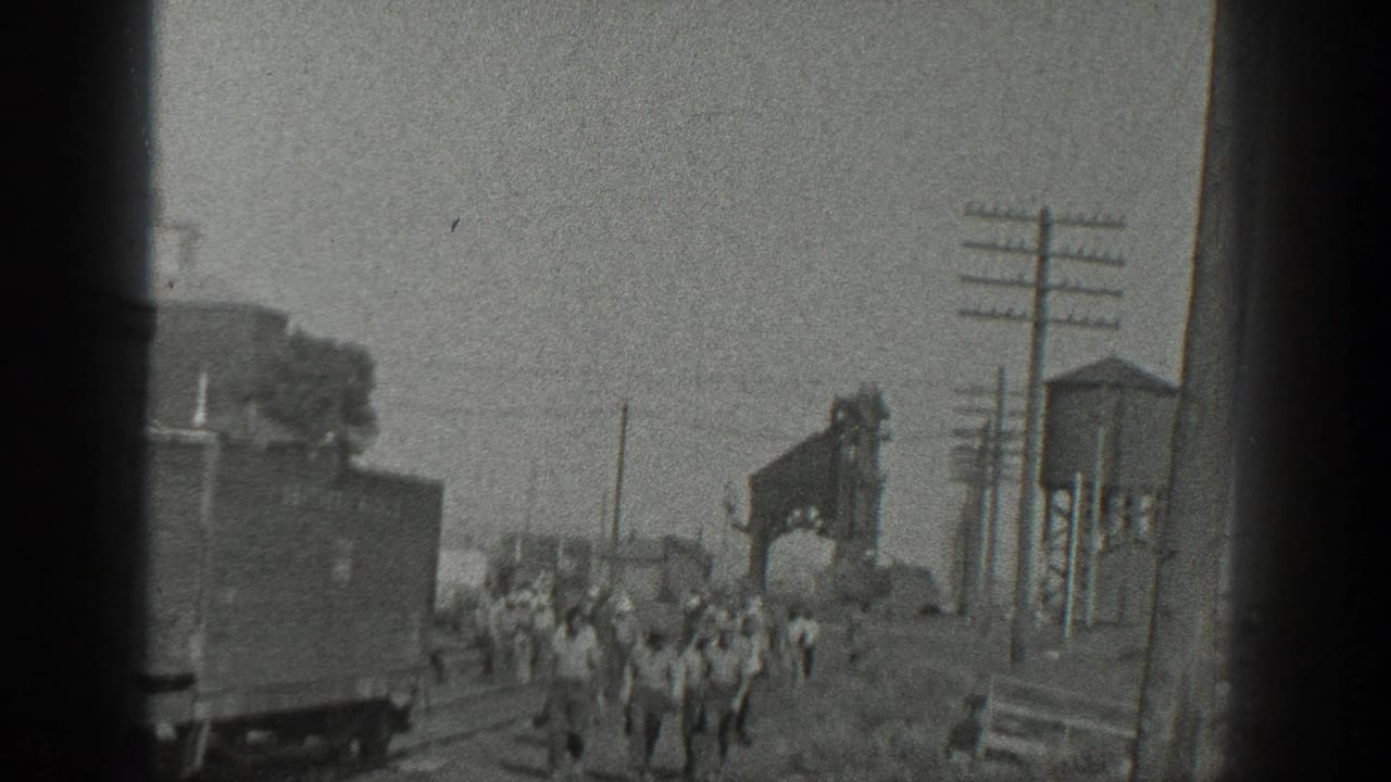 1936 California frame with workers walking through a rail yard beside tracks, a freight car, utility poles, and industrial equipment.