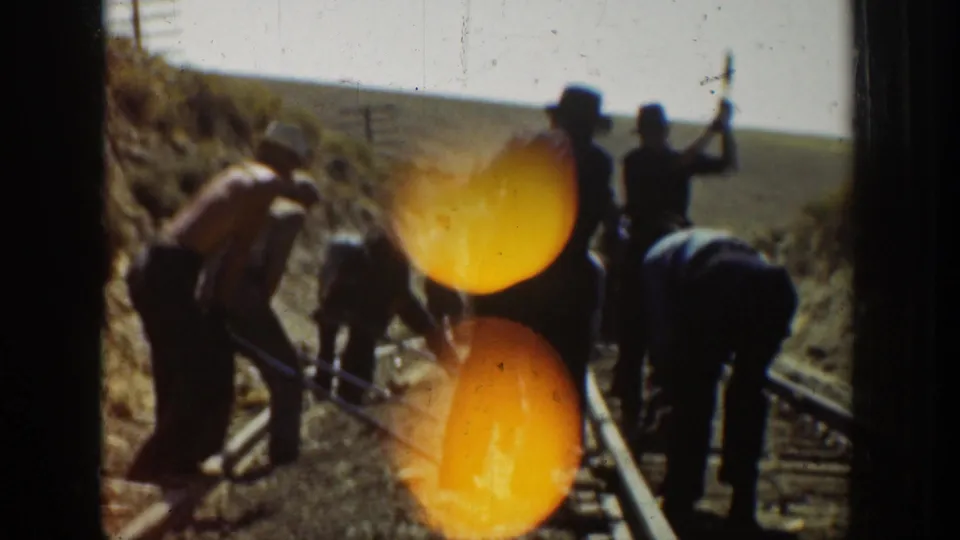 Color 8mm frame from the 1936 California clip showing workers using hand tools on railroad tracks near an open hillside.