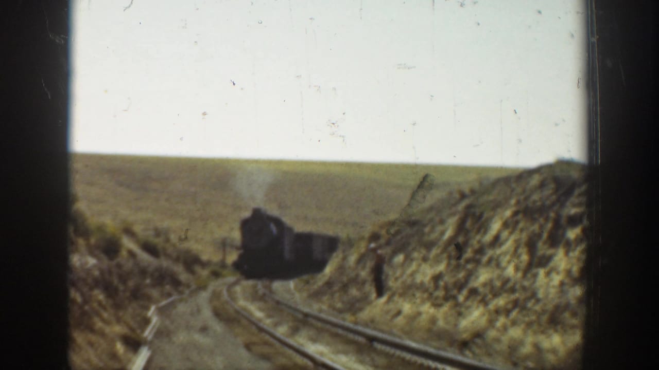 Steam locomotive approaches on a rural California rail line, framed by dry banks and open countryside in 1936 home-movie footage.
