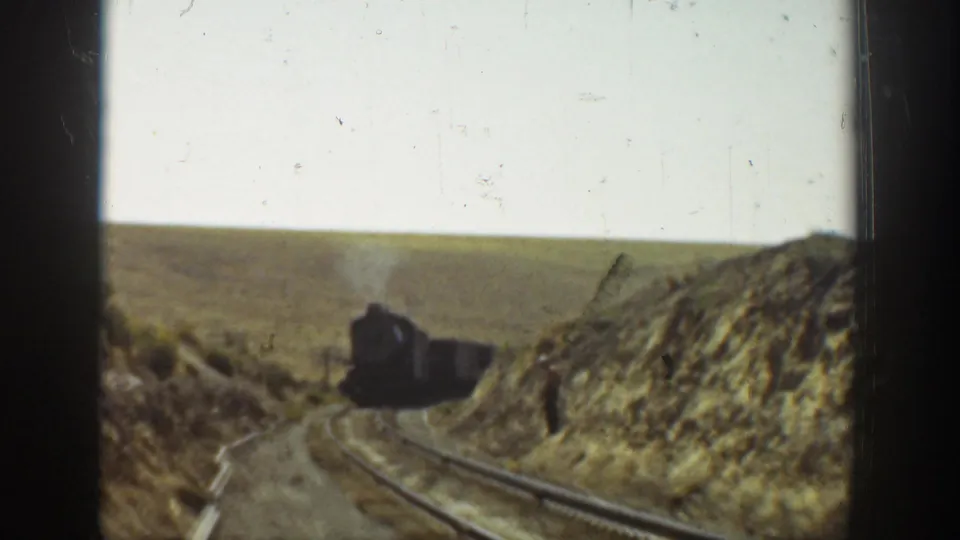 Steam locomotive approaches on a rural California rail line, framed by dry banks and open countryside in 1936 home-movie footage.