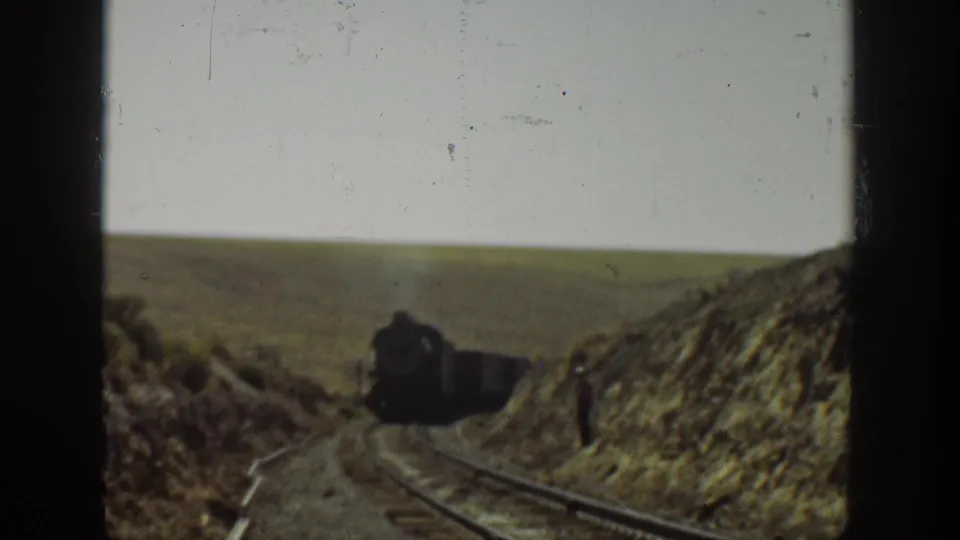 The train advances through a dry rural rail cutting in California, with rails, dirt roadbed, and open land visible around it.
