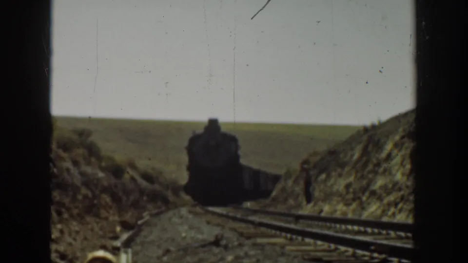 Closeer view of the approaching steam locomotive on a rural California track, with dry embankments and rail ties visible.