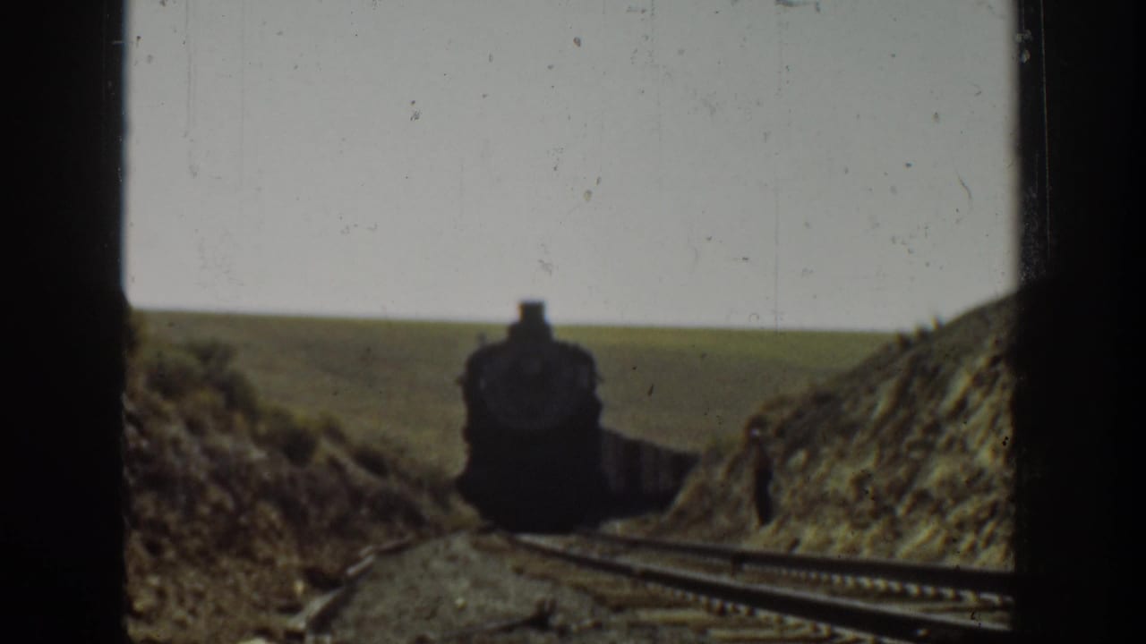1936 California 8mm frame showing a steam locomotive approaching on rural tracks through a dry hilly cut.
