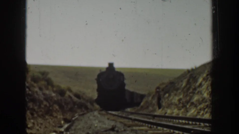 1936 California 8mm frame showing a steam locomotive approaching on rural tracks through a dry hilly cut.