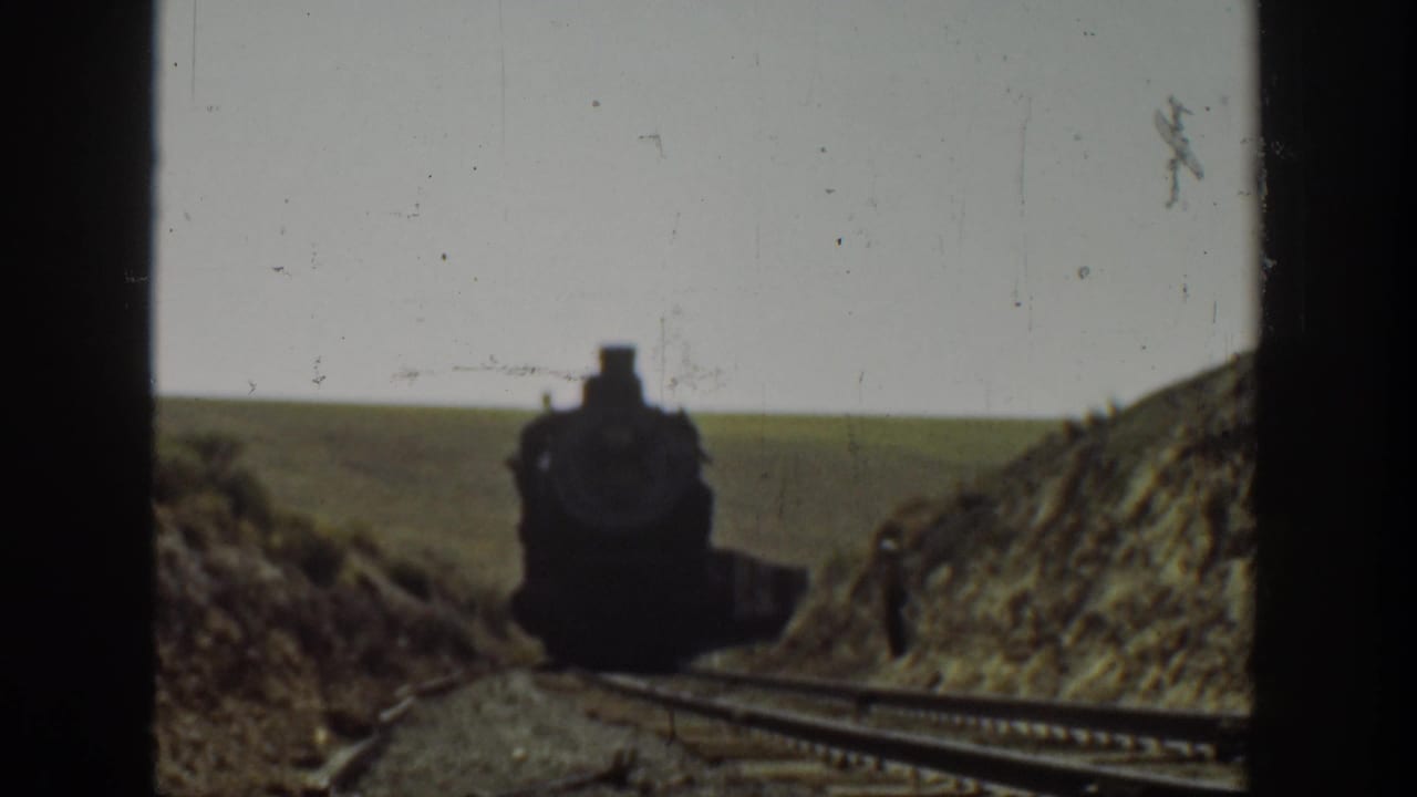 Steam locomotive moves closer along tracks with a small figure near the right side.
