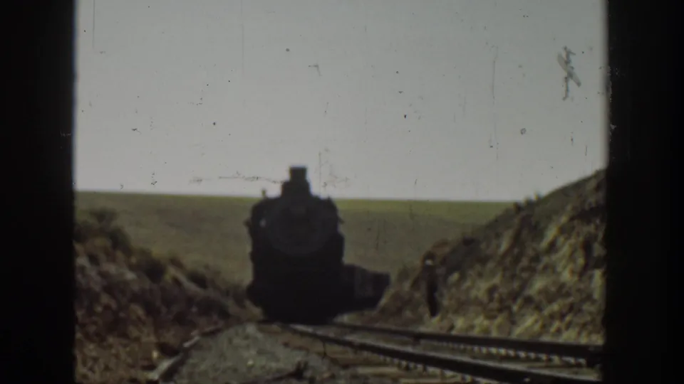 1936 California 8mm frame with a steam locomotive nearing the camera and a trackside figure by the hillside.