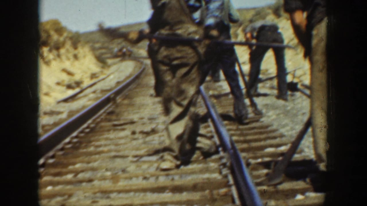 1936 California home-movie frame showing adult men using tools along railroad rails and ties in dry open terrain.