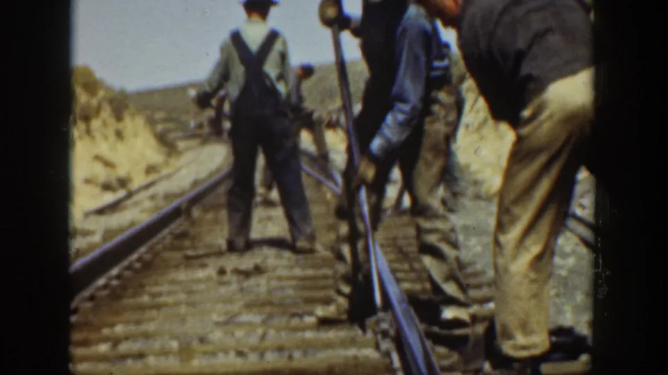 1936 California 8mm frame with men in work clothes and overalls standing along a railroad track in a dry landscape.