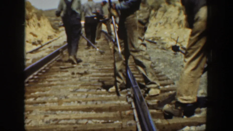 Close 1936 California home-movie view of adult railroad workers standing on ties with tools beside the rails.