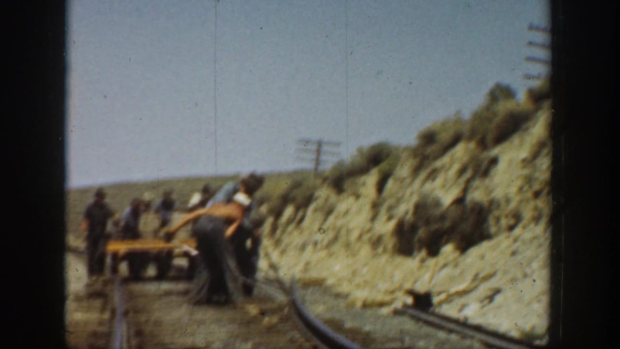 1936 California 8mm frame showing workers along railway tracks beside an arid cut bank and sparse scrub.