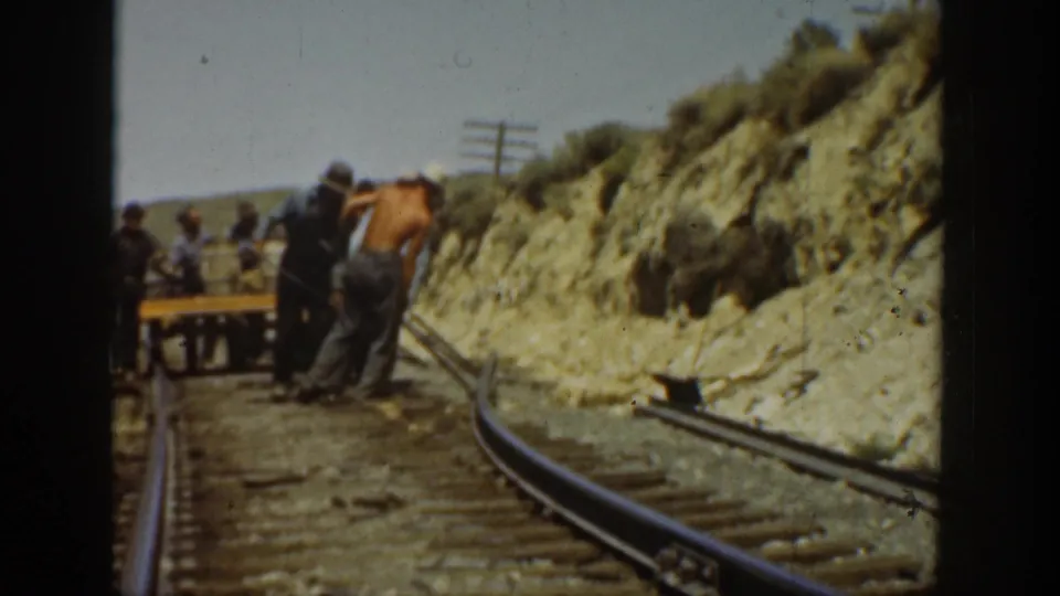 1936 California home-movie frame with rail workers clustered near a small track cart and tools on a rugged rail line.