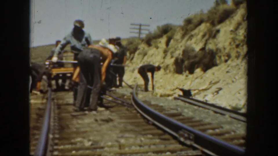 Railroad workers in 1936 California appear to repair or adjust track beside a rocky embankment and sparse vegetation.