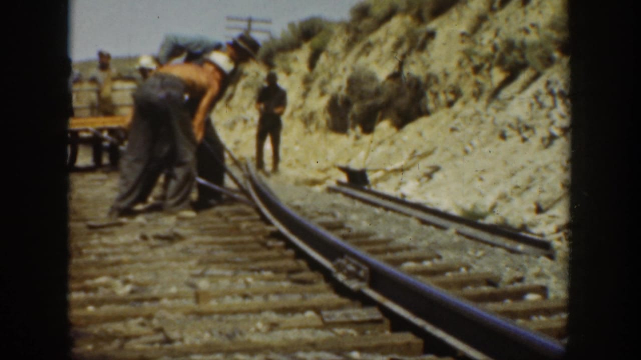 Adult men in hats and work pants bend over a steel rail on a California railroad bed in 1936 footage.