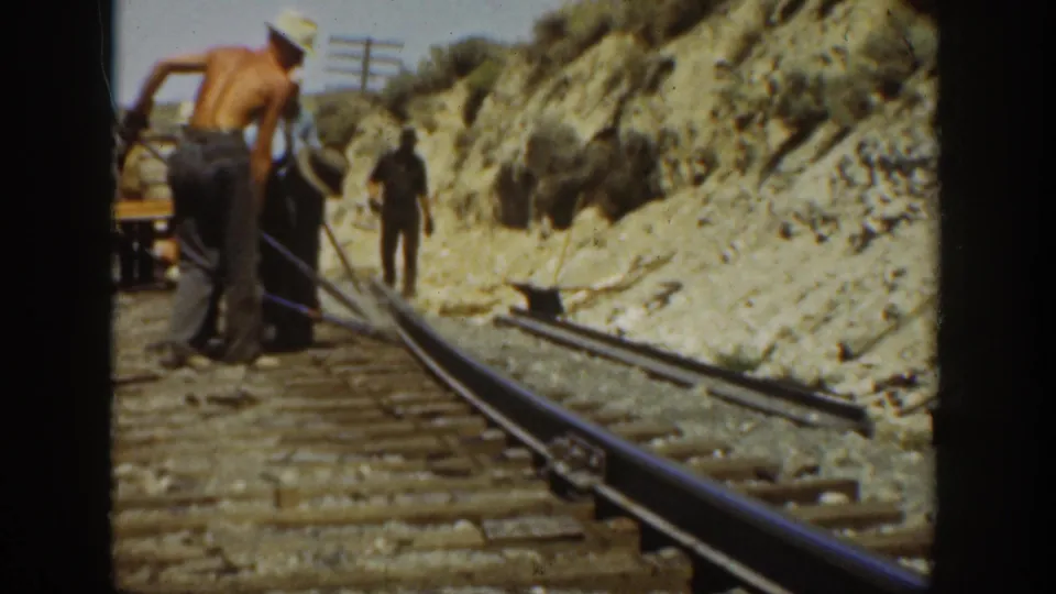 1936 California home-movie frame showing a shirtless adult worker near men repairing or adjusting a railroad track.