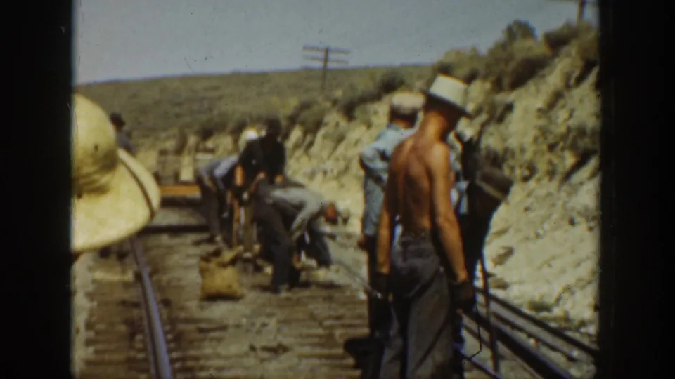 Adult railroad workers in 1936 California footage stand and crouch along rails beside a dry hillside.
