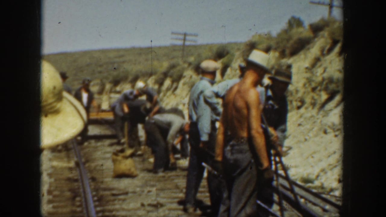 1936 California home-movie frame showing men in hats working beside railroad tracks in a dry mountain area.