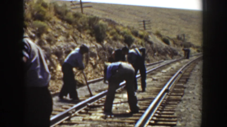 A close home-movie view shows men working by railroad rails in an arid California mountain setting.