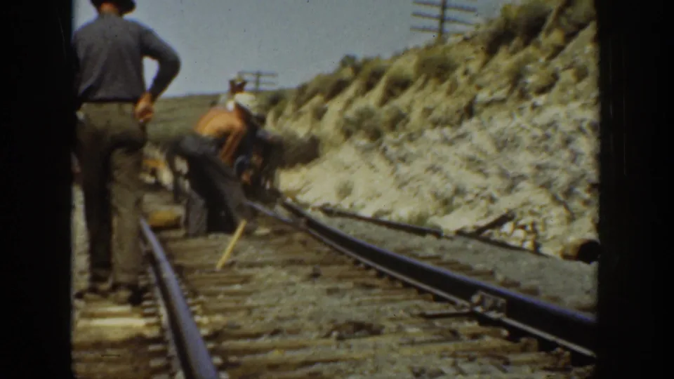 A standing man looks over track work as others use tools on railroad rails in 1936 California footage.
