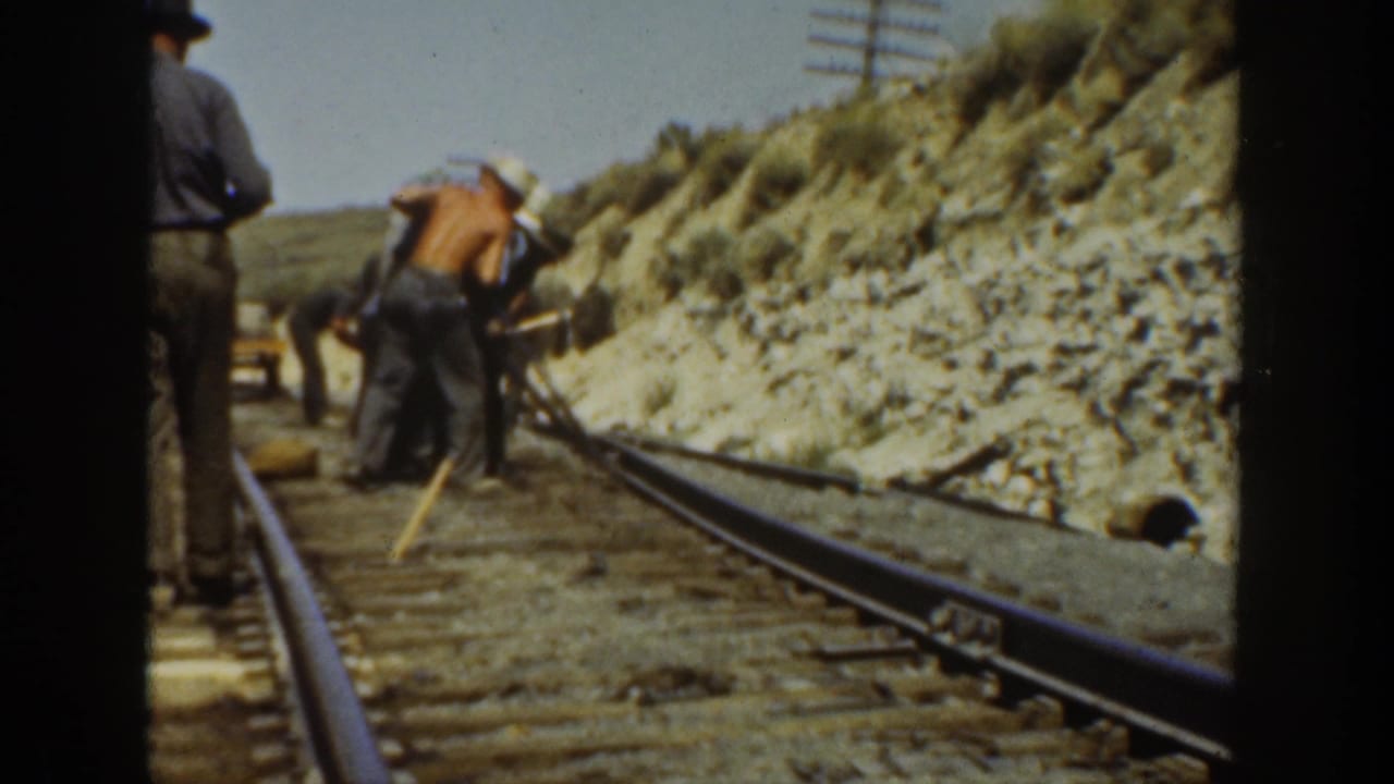 1936 California 8mm frame showing railroad workers with hand tools beside rails in a rocky cut, viewed from a moving train.