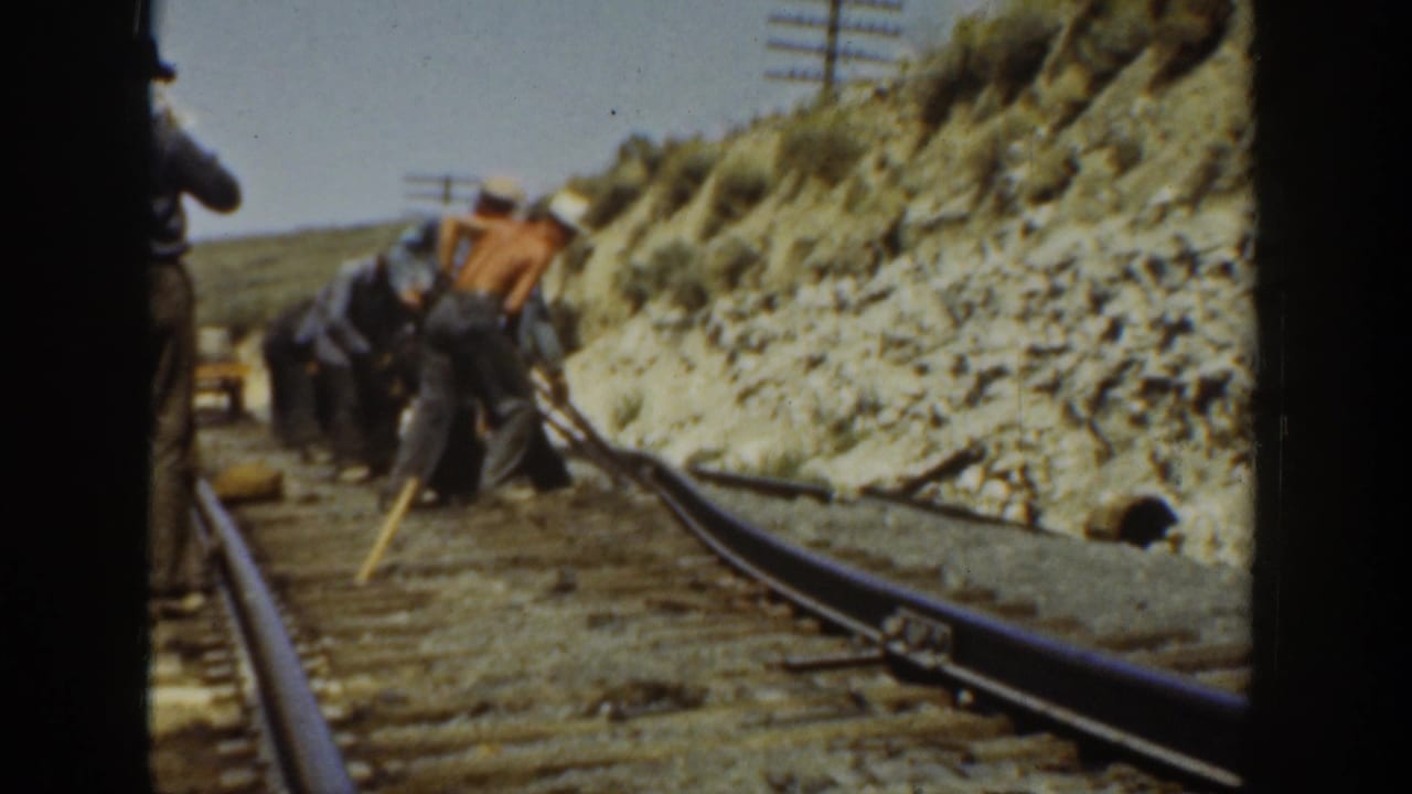 1936 California 8mm frame showing men with tools working beside railroad tracks in an arid landscape.