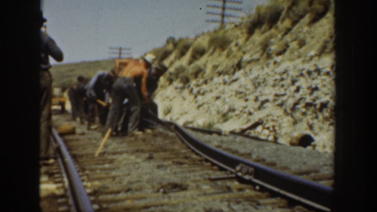 Men in work clothes adjust or tamp a railroad track in 1936 California, seen through a dark train-side frame.