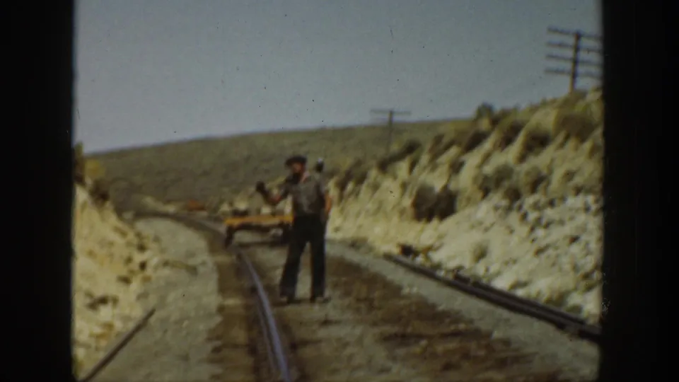 1936 California rail scene with one worker standing near tools and a curving track in an arid landscape.