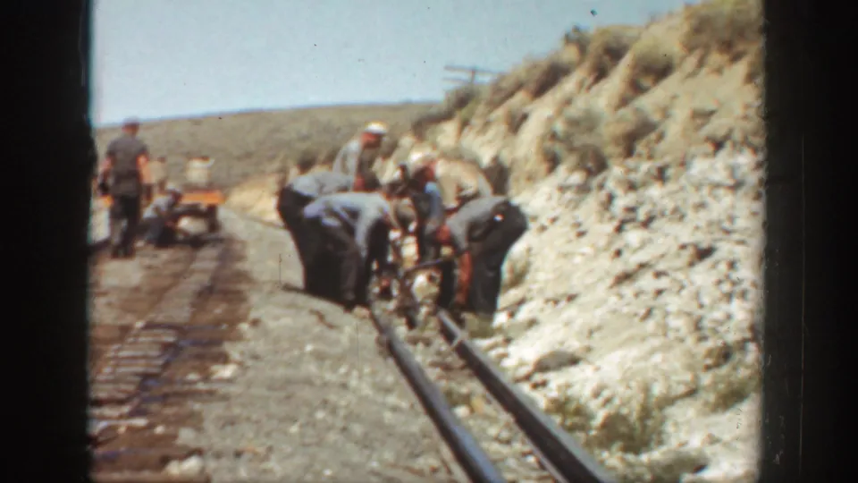 1936 California rail crew bends over a track through a dry hillside cut, with rails, ballast, workers, and small equipment visible.