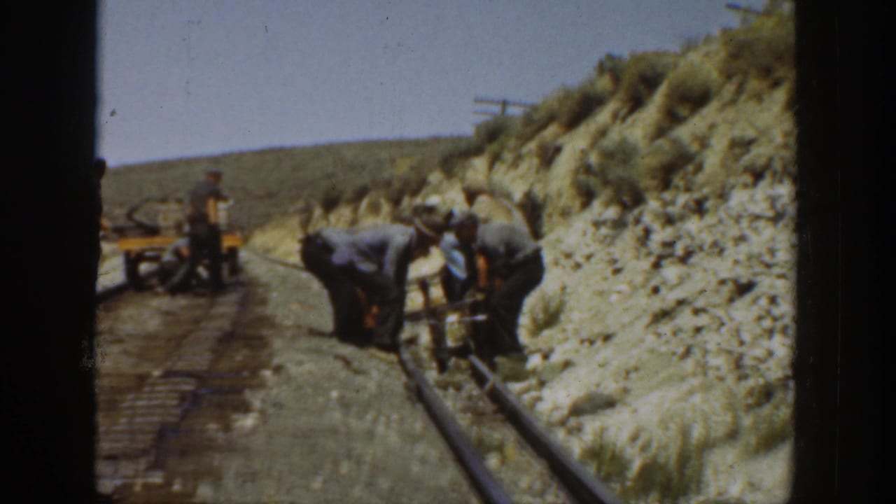 Group of men gathered around rails with a small rail cart behind them in a dry landscape.