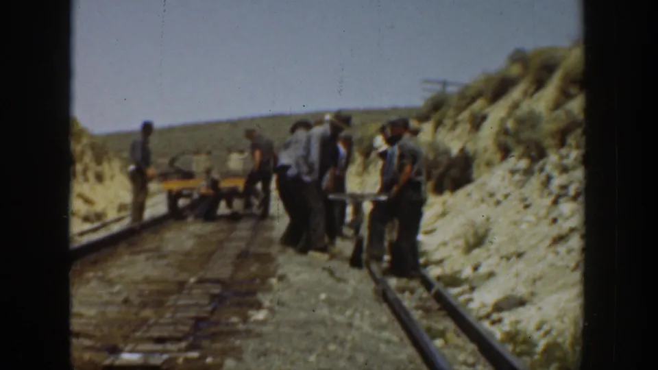 1936 California home-movie view of men positioning themselves around rails and ties, with a small track cart on the graded rail bed.