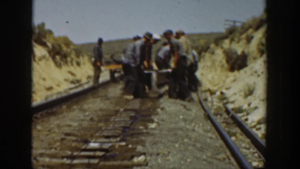 1936 California frame showing several men lifting or adjusting rail material beside exposed ties in a dry hillside construction setting.