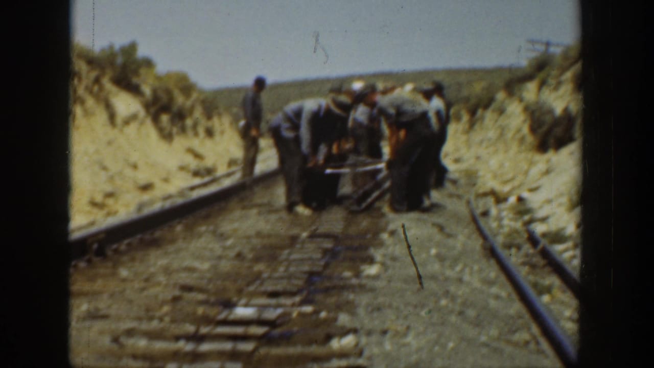 In 1936 California 8mm footage, several men work over railroad tracks between sandy embankments as one man stands beside the rail line.