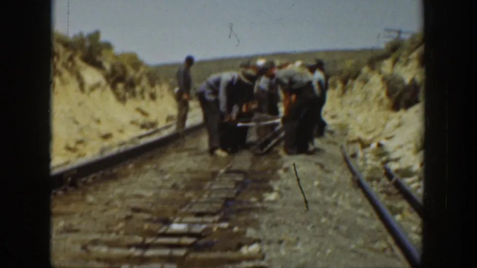 In 1936 California 8mm footage, several men work over railroad tracks between sandy embankments as one man stands beside the rail line.