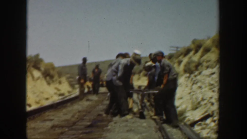 A small 1936 railroad work crew stands and bends near the rails, filmed from a handheld 8mm perspective in California.