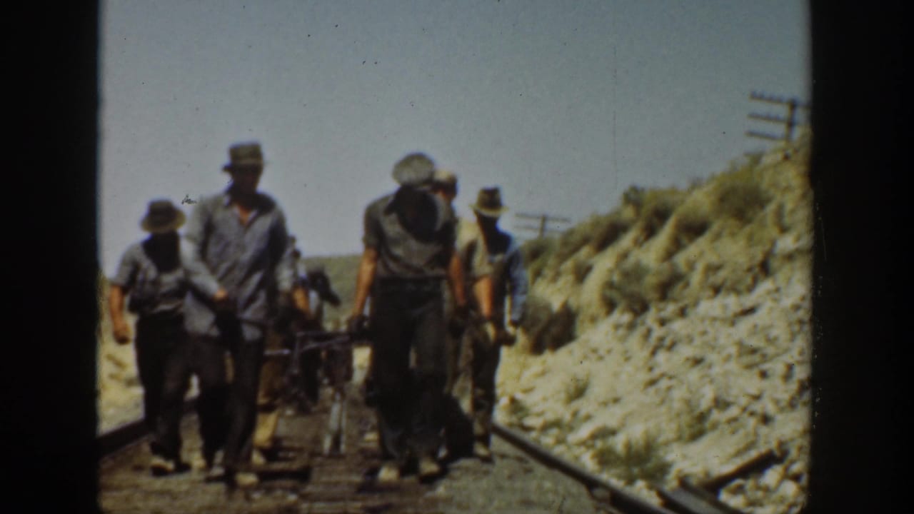 1936 California 8mm frame showing adult men in work clothes walking along railway tracks in a bright, dry landscape.