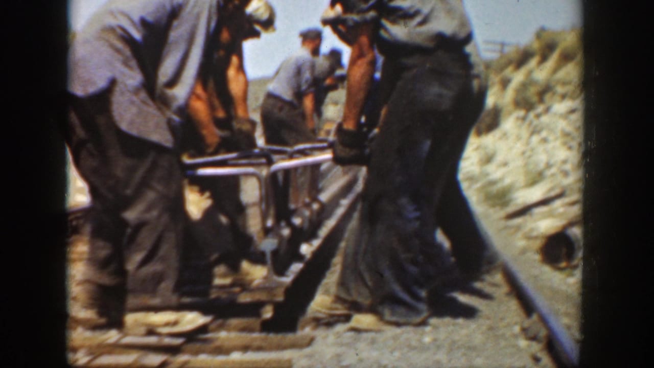 Workers in hats and denim appear to position track hardware along a rail bed in California archival footage.
