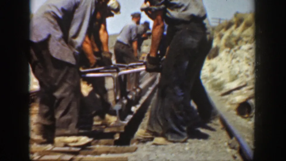 Workers in hats and denim appear to position track hardware along a rail bed in California archival footage.
