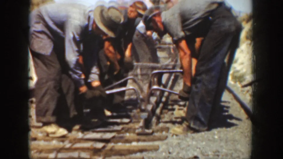 Adult workers cluster over the track, using a manual tool on a rail line in 1936 California footage.