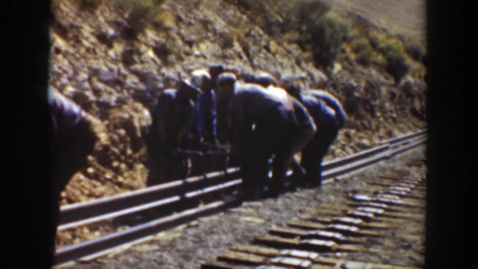 Men bend over railroad rails and ties in the dry California cut, suggesting manual track placement or adjustment work.