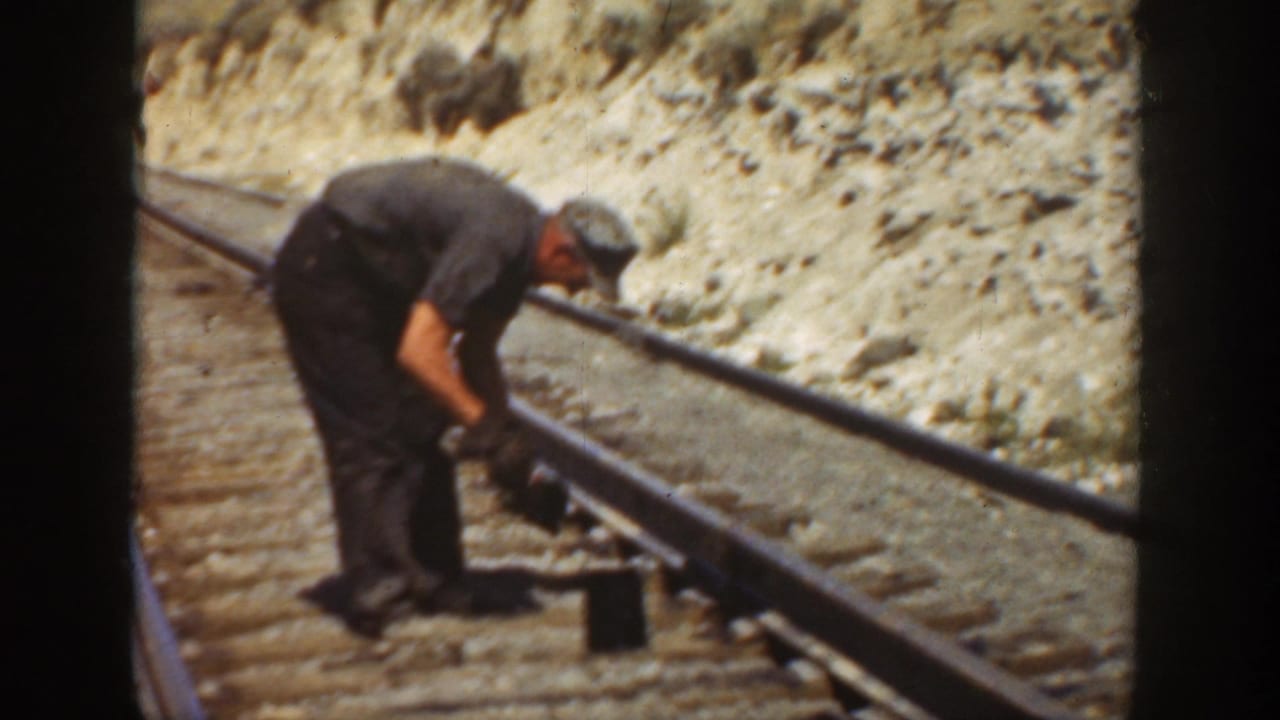 In 1936 California footage, a railroad worker in dark clothes bends over the rail while working near wooden ties and dry earth.
