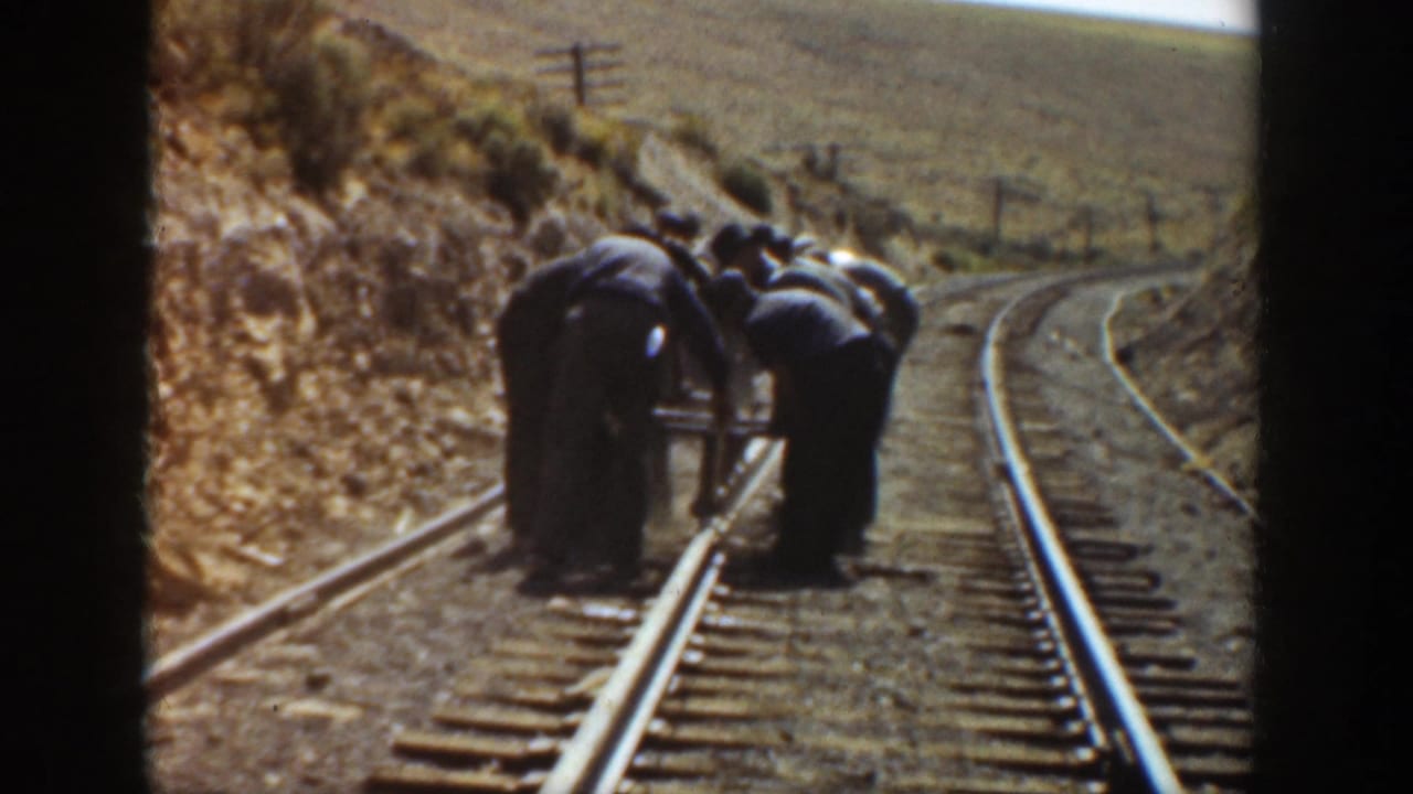 In 1936 California, several railroad workers bend over rails and ties on a dry hillside track.
