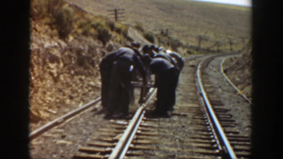 In 1936 California, several railroad workers bend over rails and ties on a dry hillside track.