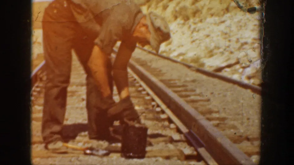 Workers stand close to the rails with tools and a container nearby during track repair in the 1936 California clip.