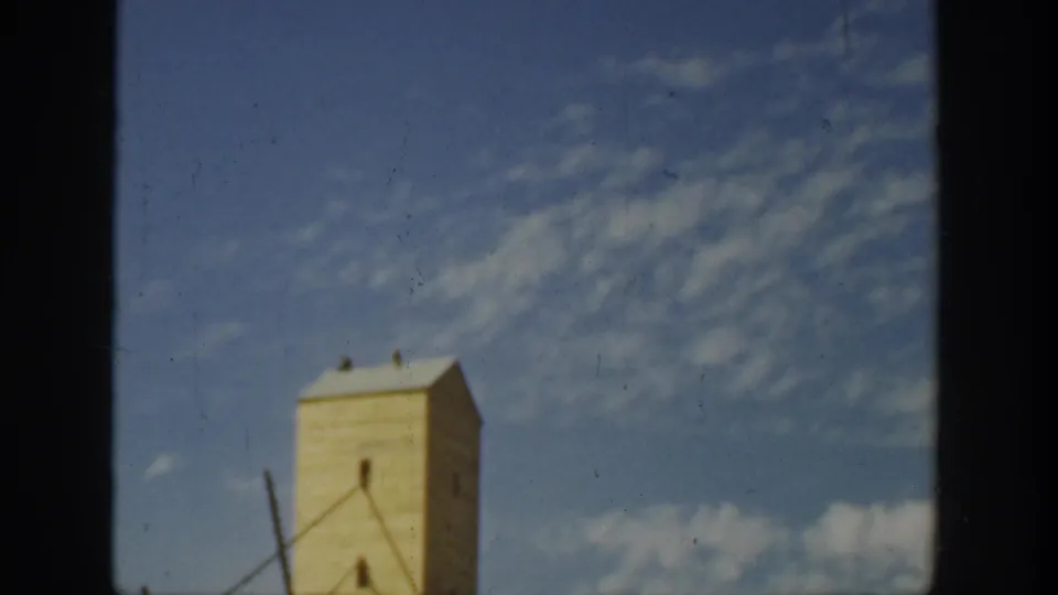 Tall rural farm structure, possibly a storage or utility building, stands against a blue California sky in 1930s home-movie footage.