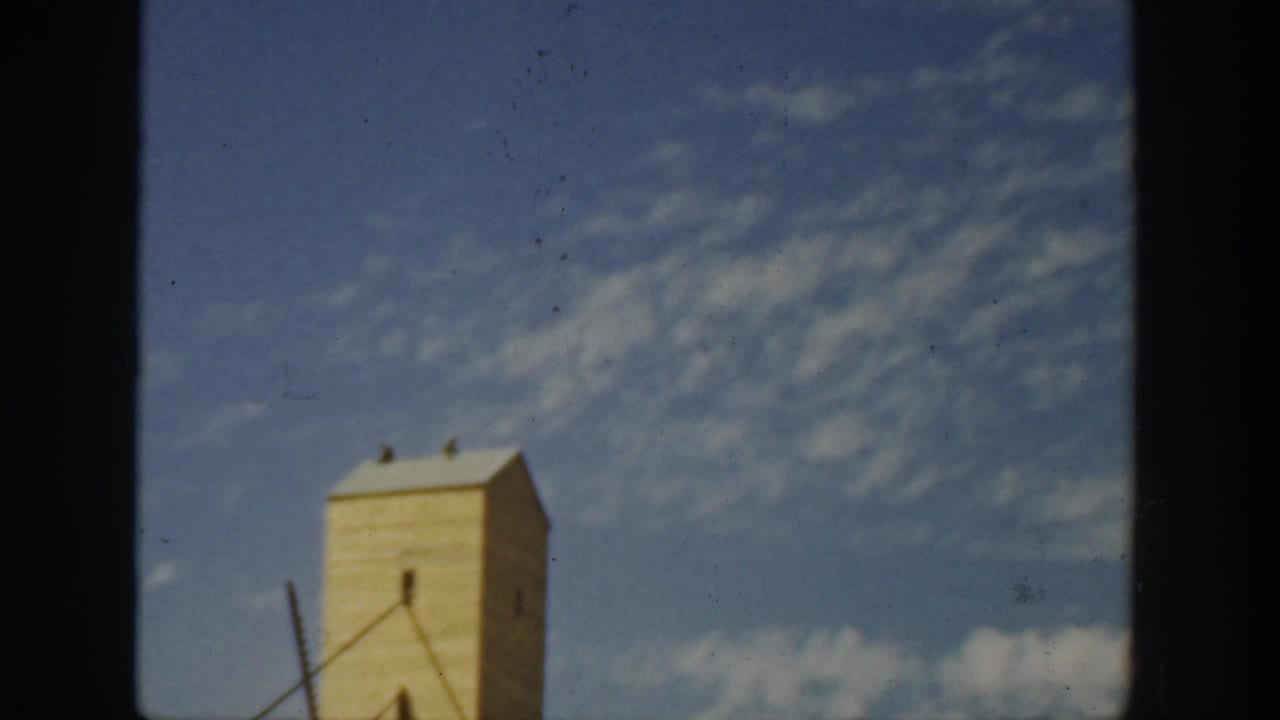 1936 California home-movie frame showing the upper portion of a tall industrial tower against a blue sky.